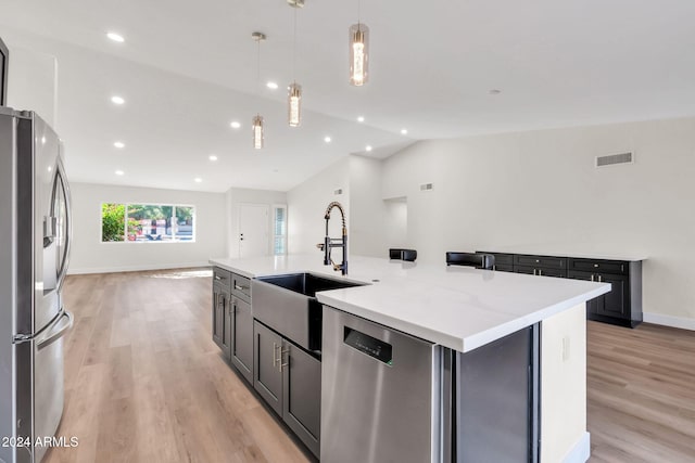 kitchen with a center island with sink, stainless steel appliances, pendant lighting, sink, and lofted ceiling