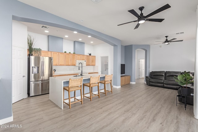 kitchen with a breakfast bar, light brown cabinets, stainless steel fridge with ice dispenser, light hardwood / wood-style floors, and an island with sink