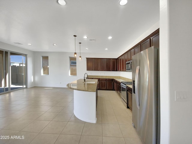 kitchen featuring sink, hanging light fixtures, an island with sink, stainless steel appliances, and light stone countertops