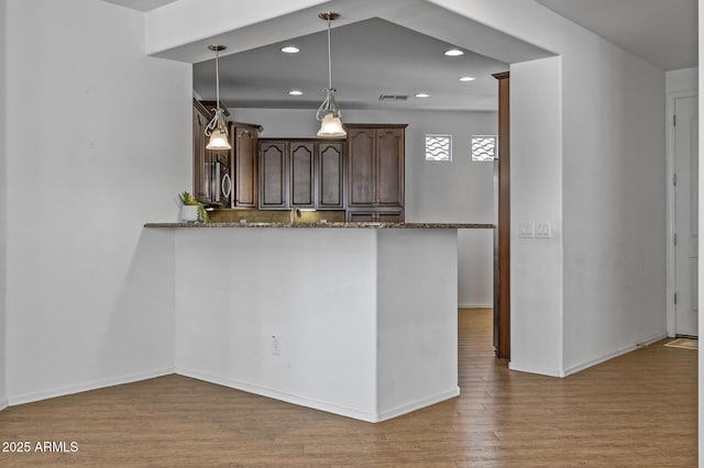 301 S 225th Ave, Buckeye, AZ 85326 - kitchen with dark brown cabinetry, visible vents, dark stone countertops, wood finished floors, and hanging light fixtures