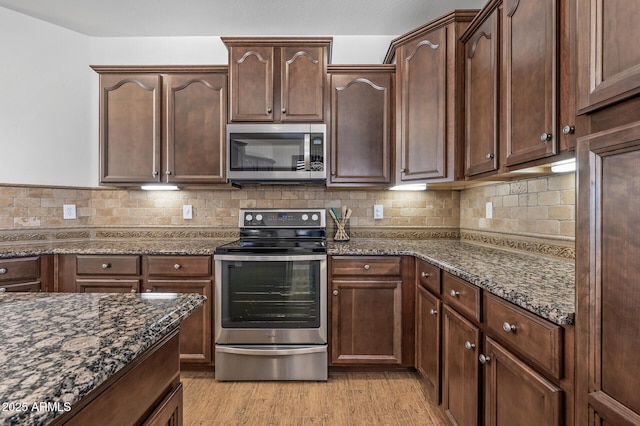301 S 225th Ave, Buckeye, AZ 85326 - kitchen with light wood-type flooring, backsplash, dark stone counters, and appliances with stainless steel finishes