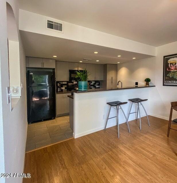 kitchen with kitchen peninsula, black refrigerator, gray cabinets, backsplash, and light wood-type flooring