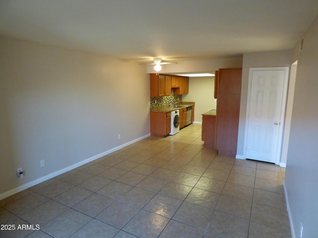 unfurnished living room with a ceiling fan, light tile patterned floors, a sink, baseboards, and washer / dryer