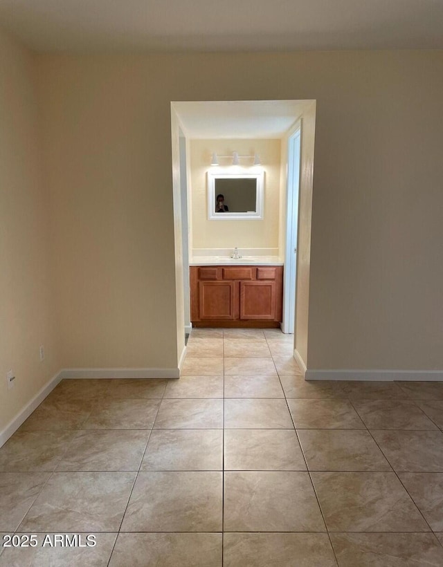 hallway featuring light tile patterned floors, baseboards, and a sink