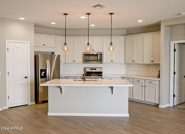 kitchen with white cabinets, light hardwood / wood-style flooring, an island with sink, and appliances with stainless steel finishes