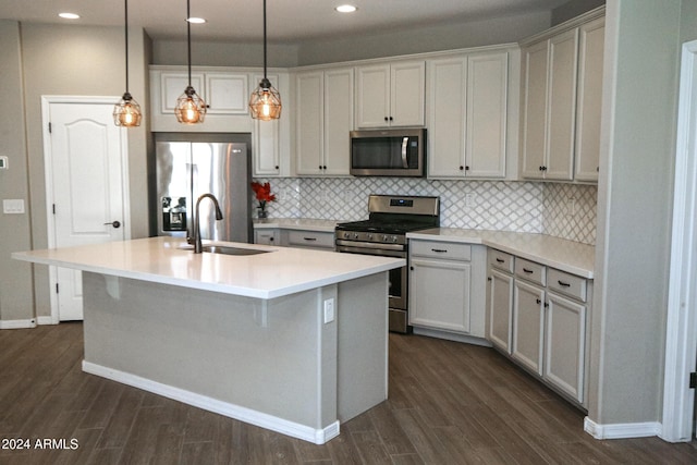 kitchen featuring a center island with sink, appliances with stainless steel finishes, pendant lighting, dark wood-type flooring, and sink