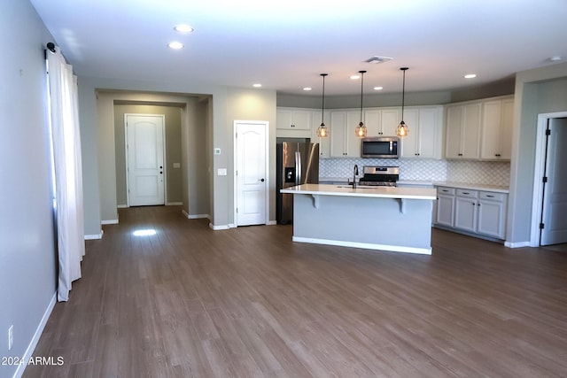 kitchen featuring dark wood-type flooring, decorative light fixtures, stainless steel appliances, tasteful backsplash, and a kitchen island with sink