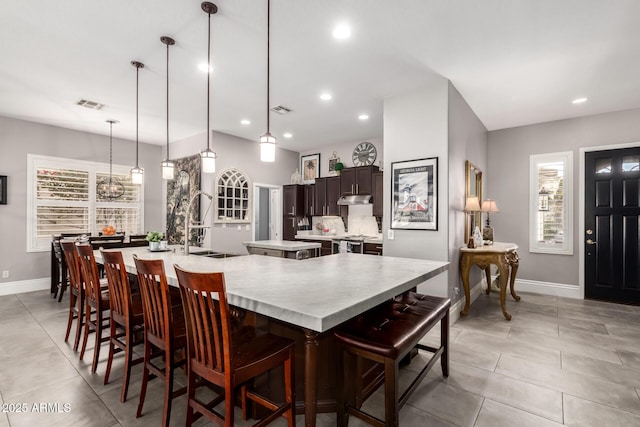 kitchen featuring pendant lighting, a large island with sink, dark brown cabinetry, stainless steel stove, and a breakfast bar area