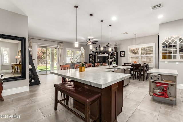 kitchen featuring dark brown cabinetry, decorative light fixtures, ceiling fan, stainless steel dishwasher, and a center island with sink