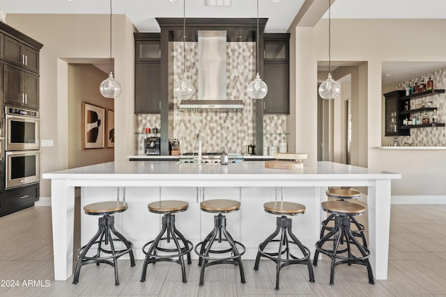 kitchen with a breakfast bar area, dark brown cabinetry, hanging light fixtures, and wall chimney range hood