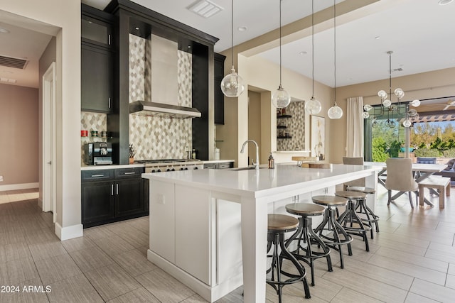 kitchen featuring decorative backsplash, sink, a kitchen island with sink, and hanging light fixtures