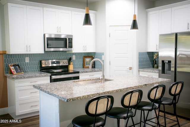 kitchen with appliances with stainless steel finishes, pendant lighting, a kitchen breakfast bar, and a sink