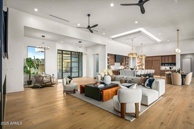 living area with ceiling fan with notable chandelier, recessed lighting, light wood-style floors, a high ceiling, and baseboards