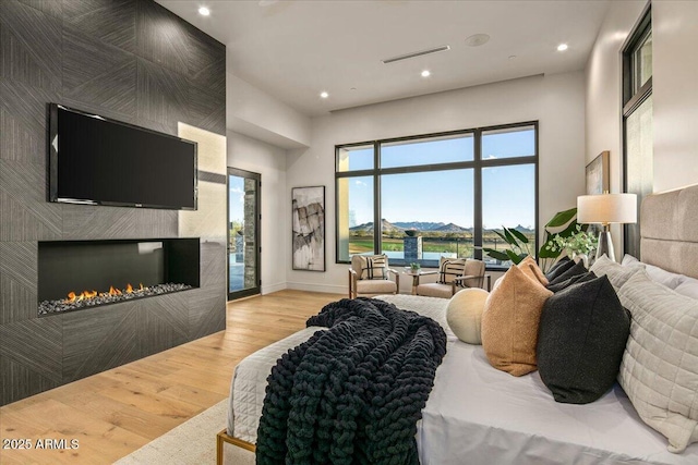 bedroom with wood finished floors, visible vents, baseboards, a fireplace, and access to outside