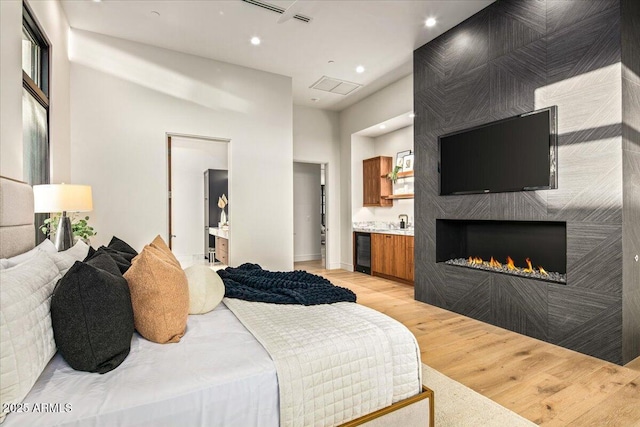 bedroom with a fireplace, ensuite bathroom, beverage cooler, and light wood finished floors