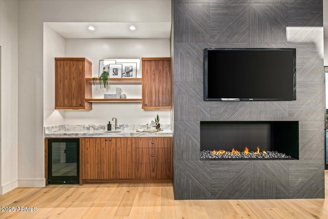 bar featuring beverage cooler, a sink, recessed lighting, a lit fireplace, and light wood finished floors