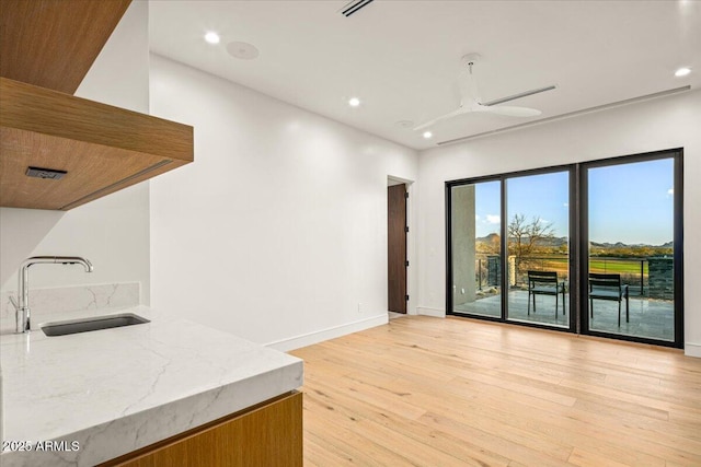 kitchen featuring light wood-style flooring, a ceiling fan, a sink, recessed lighting, and light stone countertops