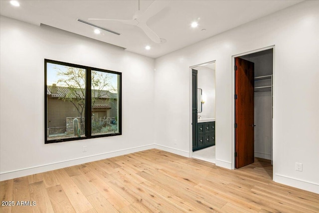 unfurnished bedroom featuring connected bathroom, baseboards, light wood-style floors, and a spacious closet