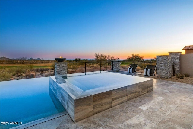 pool at dusk featuring an in ground hot tub and a patio area