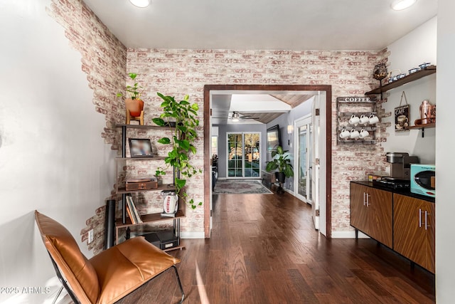 hall with dark wood-style floors, brick wall, and baseboards