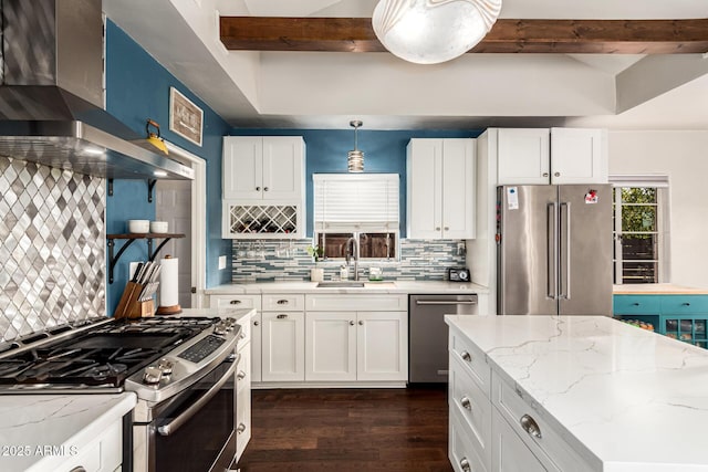 kitchen with white cabinets, appliances with stainless steel finishes, beamed ceiling, wall chimney range hood, and a sink