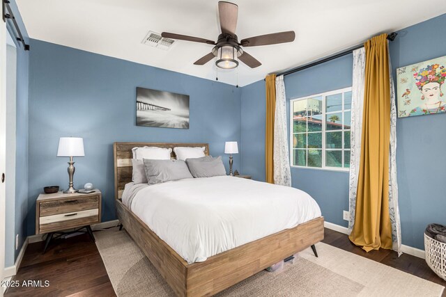 bedroom featuring a barn door, baseboards, visible vents, ceiling fan, and wood finished floors