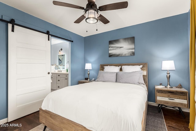 bedroom featuring ensuite bath, a barn door, ceiling fan, and wood finished floors