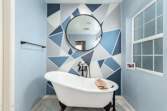 bathroom with marble finish floor, visible vents, a freestanding bath, and baseboards