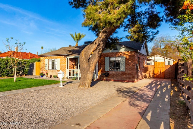 bungalow with covered porch, brick siding, fence, a gate, and a front lawn