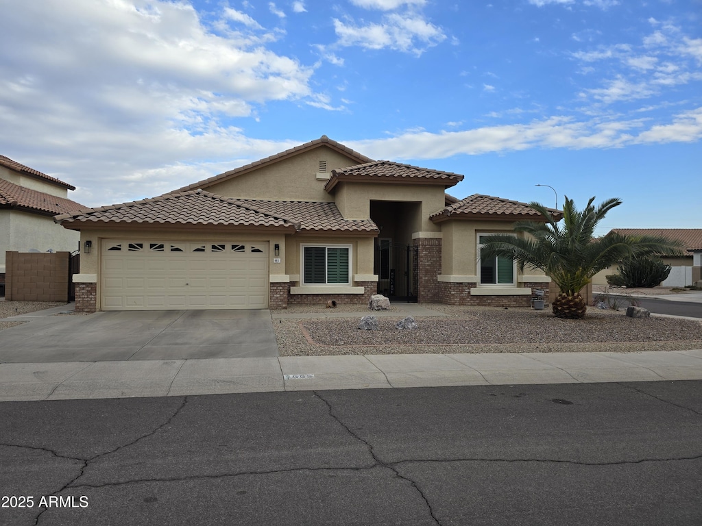 mediterranean / spanish house with a garage, driveway, brick siding, and stucco siding