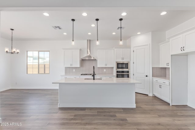 kitchen featuring light countertops, wall chimney range hood, appliances with stainless steel finishes, and white cabinets