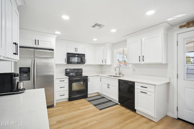 kitchen featuring visible vents, light wood-style flooring, white cabinetry, a sink, and black appliances