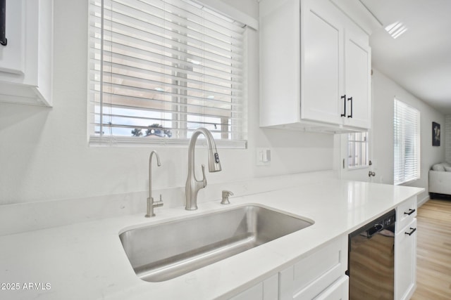 kitchen featuring light countertops, light wood-style flooring, white cabinets, a sink, and dishwasher