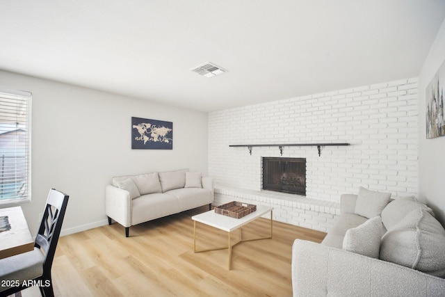 living room featuring a brick fireplace, visible vents, baseboards, and wood finished floors