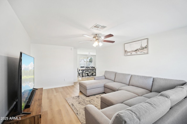 living area featuring baseboards, light wood-style flooring, visible vents, and a ceiling fan