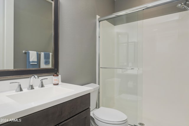 bathroom featuring a shower with shower door, vanity, and toilet