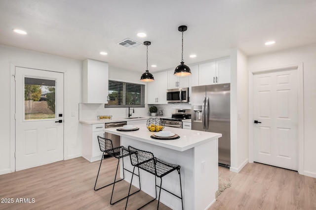 kitchen featuring white cabinetry, hanging light fixtures, light wood-type flooring, a kitchen island, and stainless steel appliances