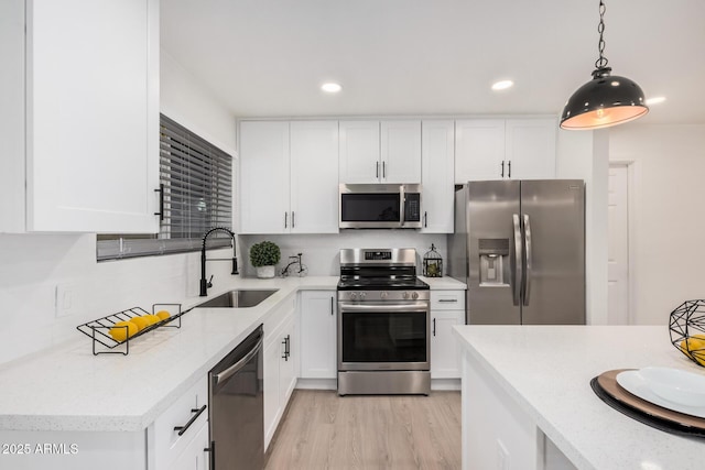 kitchen featuring appliances with stainless steel finishes, pendant lighting, white cabinetry, sink, and light hardwood / wood-style floors