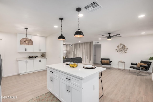 kitchen with decorative light fixtures, white cabinetry, a kitchen breakfast bar, a center island, and light hardwood / wood-style floors