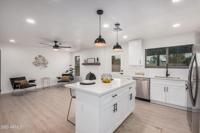 kitchen with sink, white cabinetry, a kitchen island, decorative light fixtures, and stainless steel dishwasher