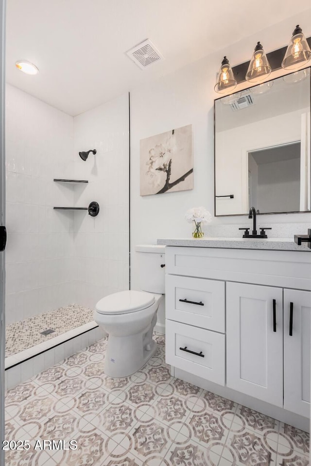 bathroom featuring vanity, tile patterned flooring, toilet, and tiled shower