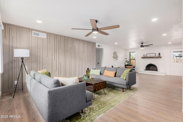 living room with ceiling fan, a fireplace, and light hardwood / wood-style flooring