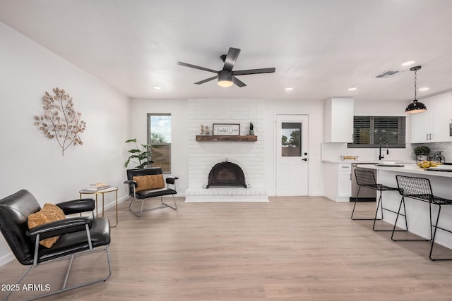 living room with a brick fireplace, sink, ceiling fan, and light wood-type flooring