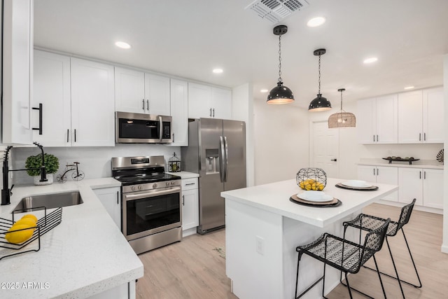 kitchen featuring appliances with stainless steel finishes, decorative light fixtures, white cabinetry, sink, and a center island