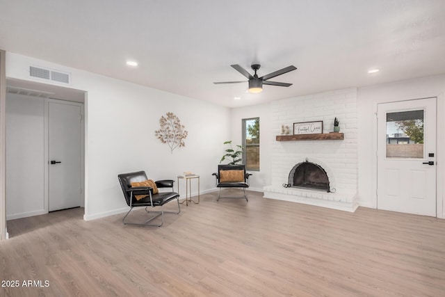 living area with ceiling fan, light wood-type flooring, and a fireplace