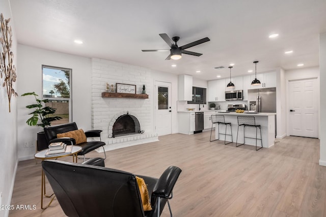 living room featuring a brick fireplace, ceiling fan, and light hardwood / wood-style flooring