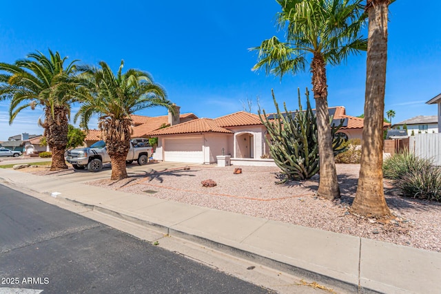 view of front of house with driveway, fence, an attached garage, a tile roof, and stucco siding