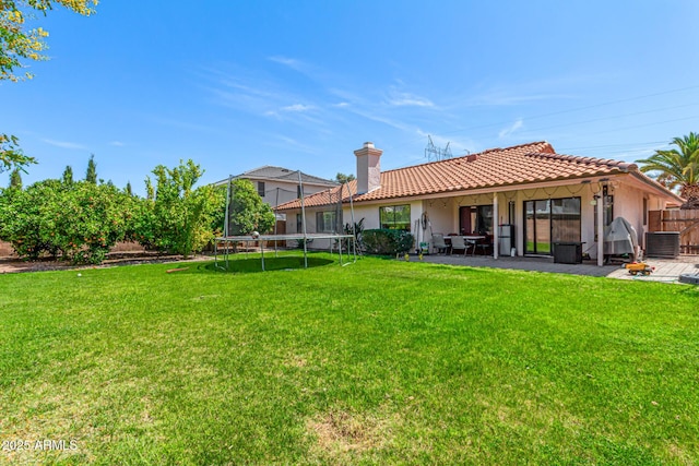back of property featuring a trampoline, fence, a patio, a tiled roof, and a yard