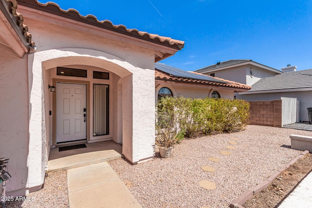view of exterior entry featuring a tiled roof, stucco siding, fence, and roof mounted solar panels