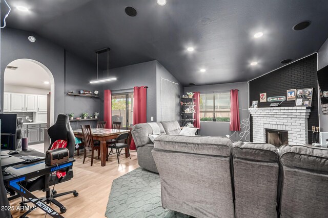 living area with vaulted ceiling, recessed lighting, arched walkways, light wood finished floors, and a brick fireplace